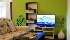 A living room with a sofa, coffee table, TV, shelves, and a vase.