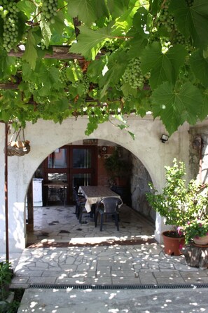 Un espace de restauration en plein air avec un sol en pierre, une table et des chaises, le tout installé sous une arche de vignes.