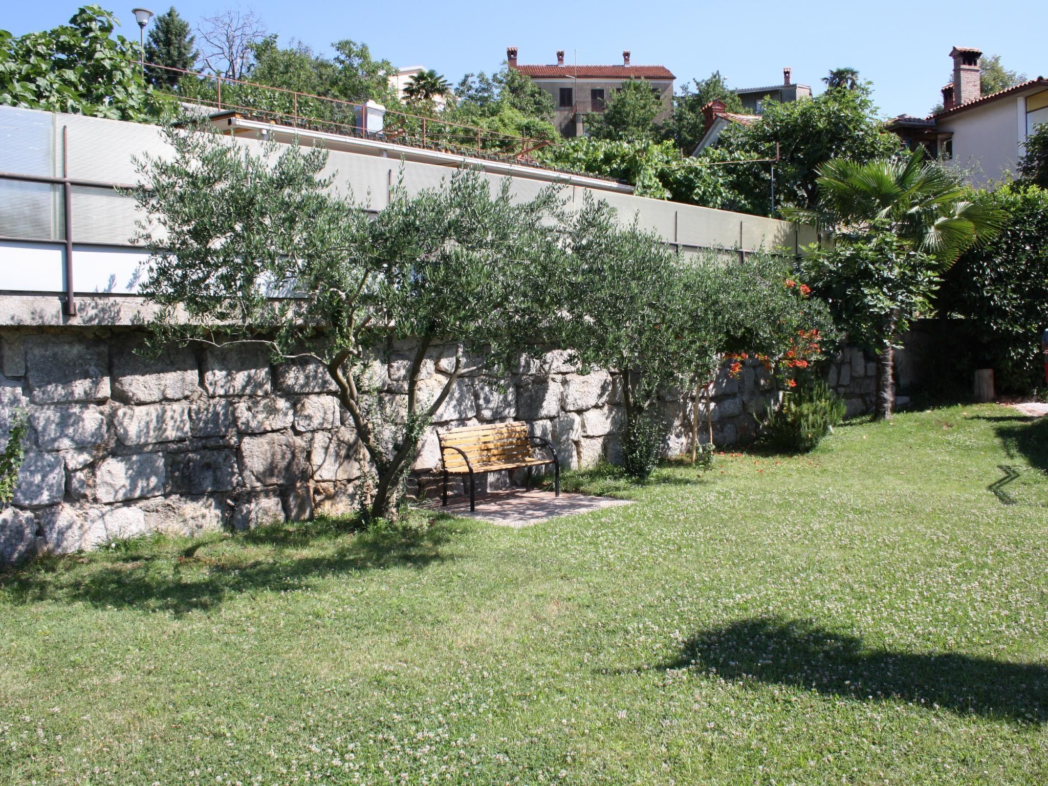 A stone wall with a bench, a grassy area, and a view of houses in the background.