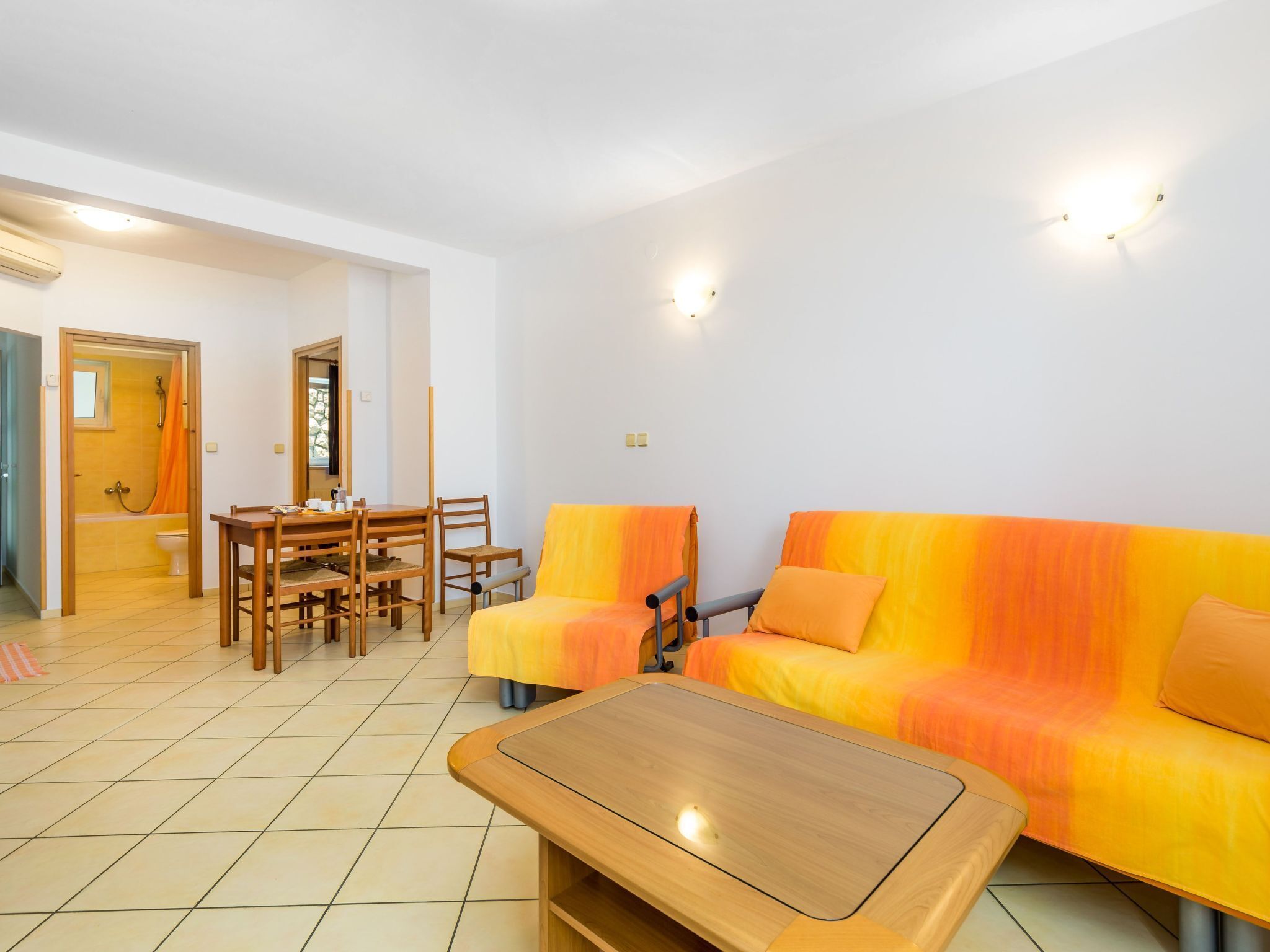 Een moderne woonkamer met een houten salontafel, een bank met oranje kussens, en een eethoek met een houten tafel en stoelen.
