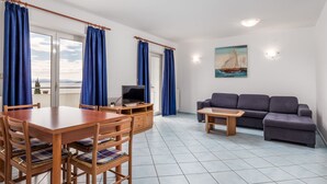 Una sala de estar con comedor, un sofá gris, un televisor sobre un mueble de madera y un cuadro de un velero en la pared.
