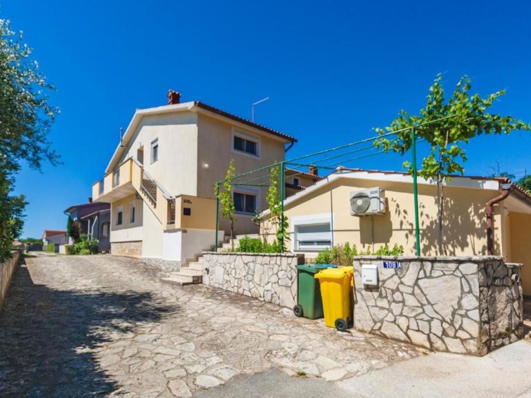 Ein zweistöckiges Haus mit einer Steintreppe zum Eingang, einem kleinen Garten und einem strahlend blauen Himmel.