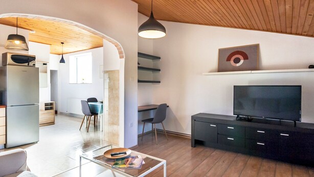 Een moderne woonkamer met een glazen salontafel, een bank, een televisie op een zwart voetstuk, en een eethoek op de achtergrond.