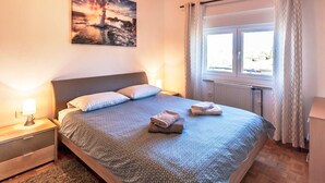 Een slaapkamer met een bed, nachtkastjes, een raam met gordijnen en een schilderij aan de muur.