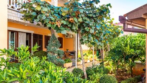 A courtyard with a variety of plants, a small tree, and a building with a balcony. - Appartement in Fažana mit Möbliertem Balkon by Interhome (Fažana)