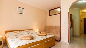 A bedroom with a wooden bed, a nightstand, a lamp, a patterned sofa, and a mirror. - Appartement in Fažana mit Möbliertem Balkon by Interhome (Fažana)
