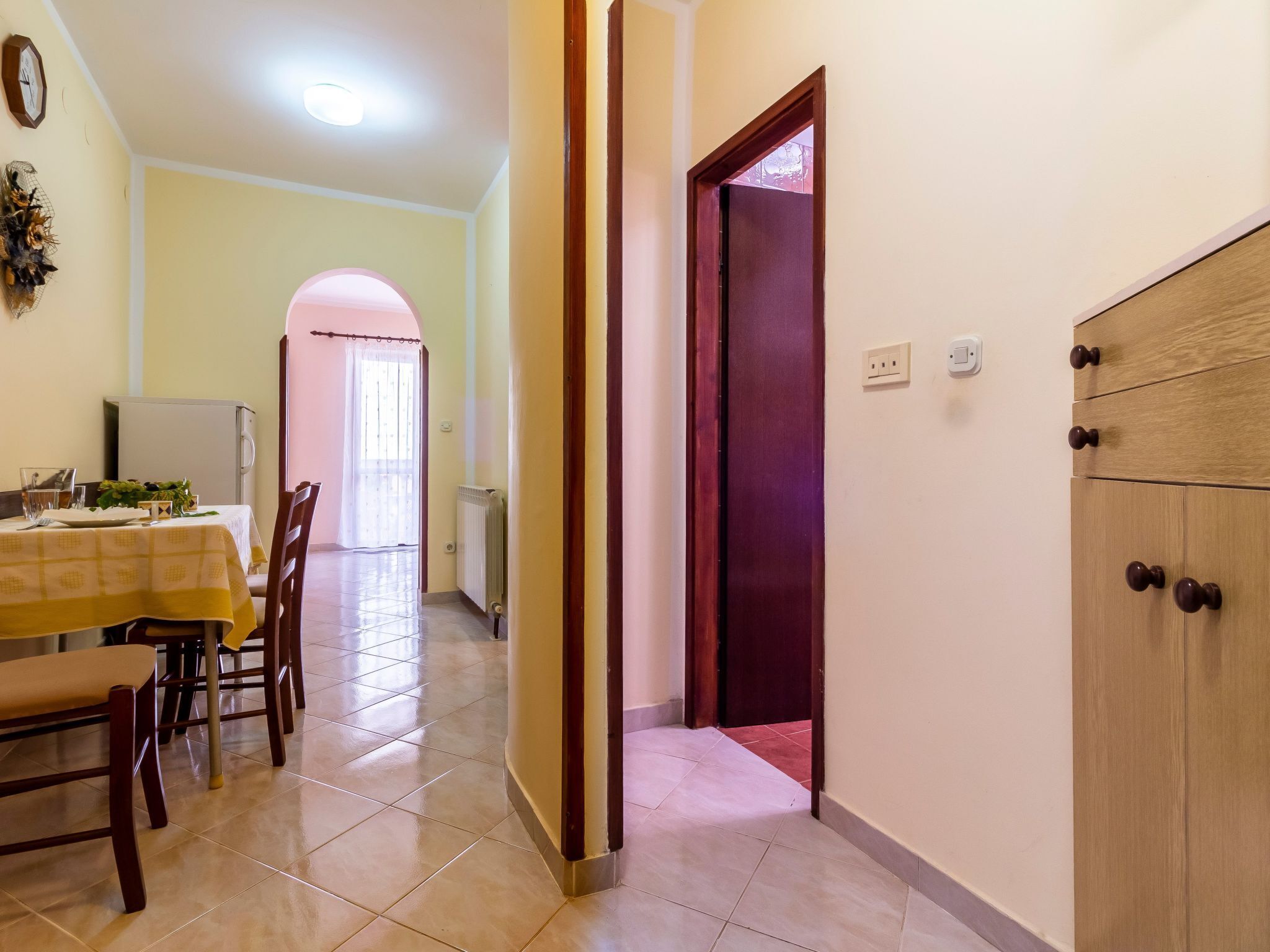 A dining area with a table set for two, a refrigerator, and a radiator.