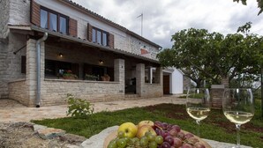 Un edificio de piedra con un balcón, una exhibición de frutas y vino, y un árbol al fondo.