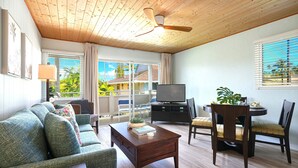Un salon avec un plafond en bois, un canapé, une table basse, un téléviseur et un coin repas comprenant des chaises et une table.