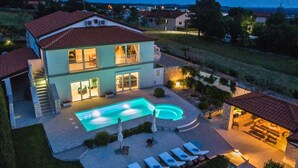 Ett hus i två våningar med en swimmingpool, utomhusmöbler och en väl upplyst uteplats.