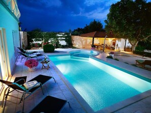 Piscina com borda curva, rodeada por espreguiçadeiras e uma mesa pequena com uma bebida.