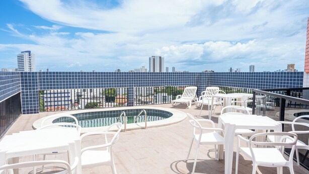 A rooftop pool area with white chairs and tables, surrounded by a blue-tiled fence, overlooking a cityscape. - Recife Center (Recife)
