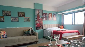 A hotel room with a teal wall, a bed with a red blanket, a sofa with a polka dot pillow, and a dining table set with glasses and plates. - Recife Center (Recife)