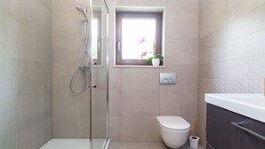 A modern bathroom with a glass-enclosed shower, a toilet, and a small window with a potted plant. - Modernes Apartment mit Balkon und Gemeinschaftsgarten am Waldrand by Interhome (Dracevac)