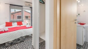 A modern hotel room with a bed, a bathroom with a sink and mirror, and a view of the outside. - in Funtana mit Grill by Interhome (Poreč/Funtana)