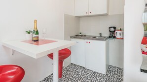 A compact kitchen with white cabinets, a small dining table, and a red stool. - in Funtana mit Grill by Interhome (Poreč/Funtana)