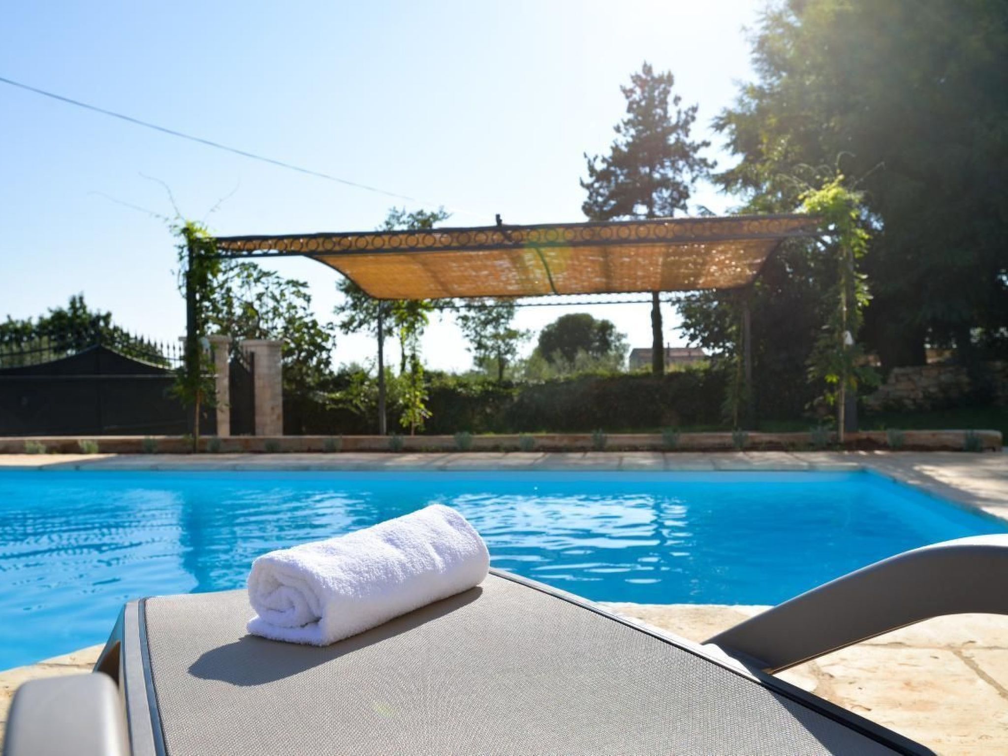 A pool area with a sunshade, a lounge chair, and a rolled towel.
