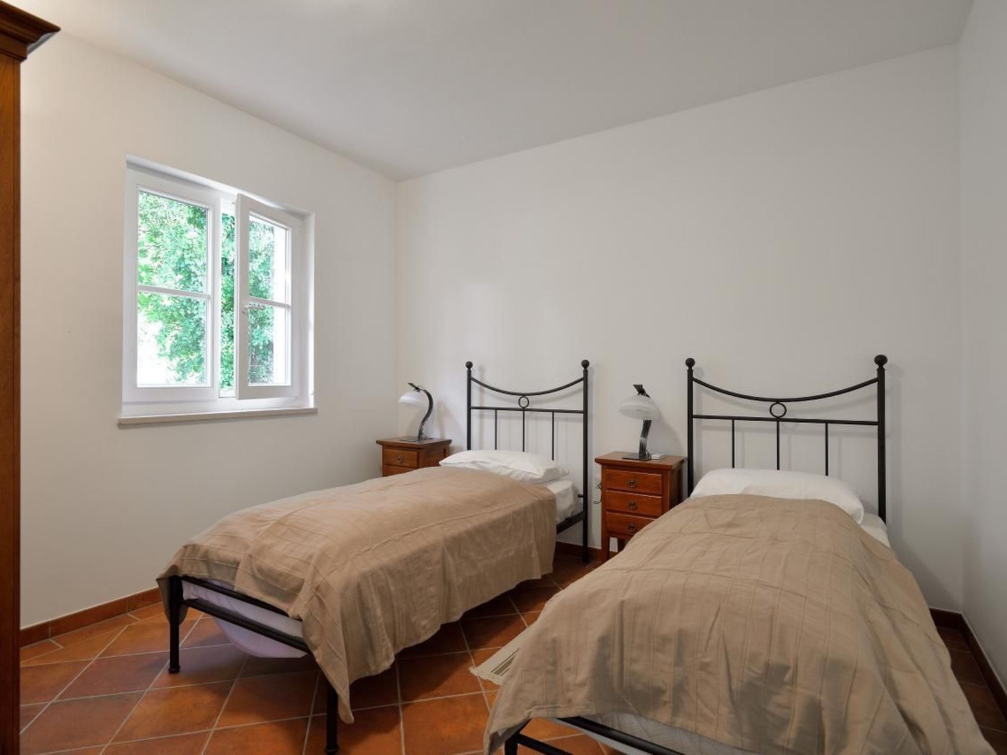 A bedroom with two single beds, a window, and a nightstand with a lamp.