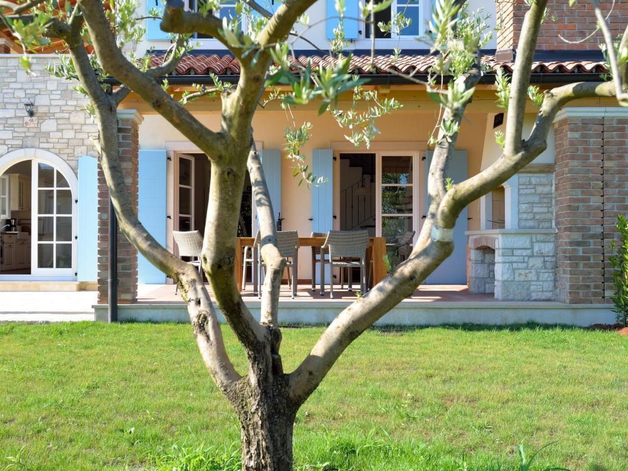 A two-story house with a stone facade, a tiled roof, and a small patio with outdoor furniture.
