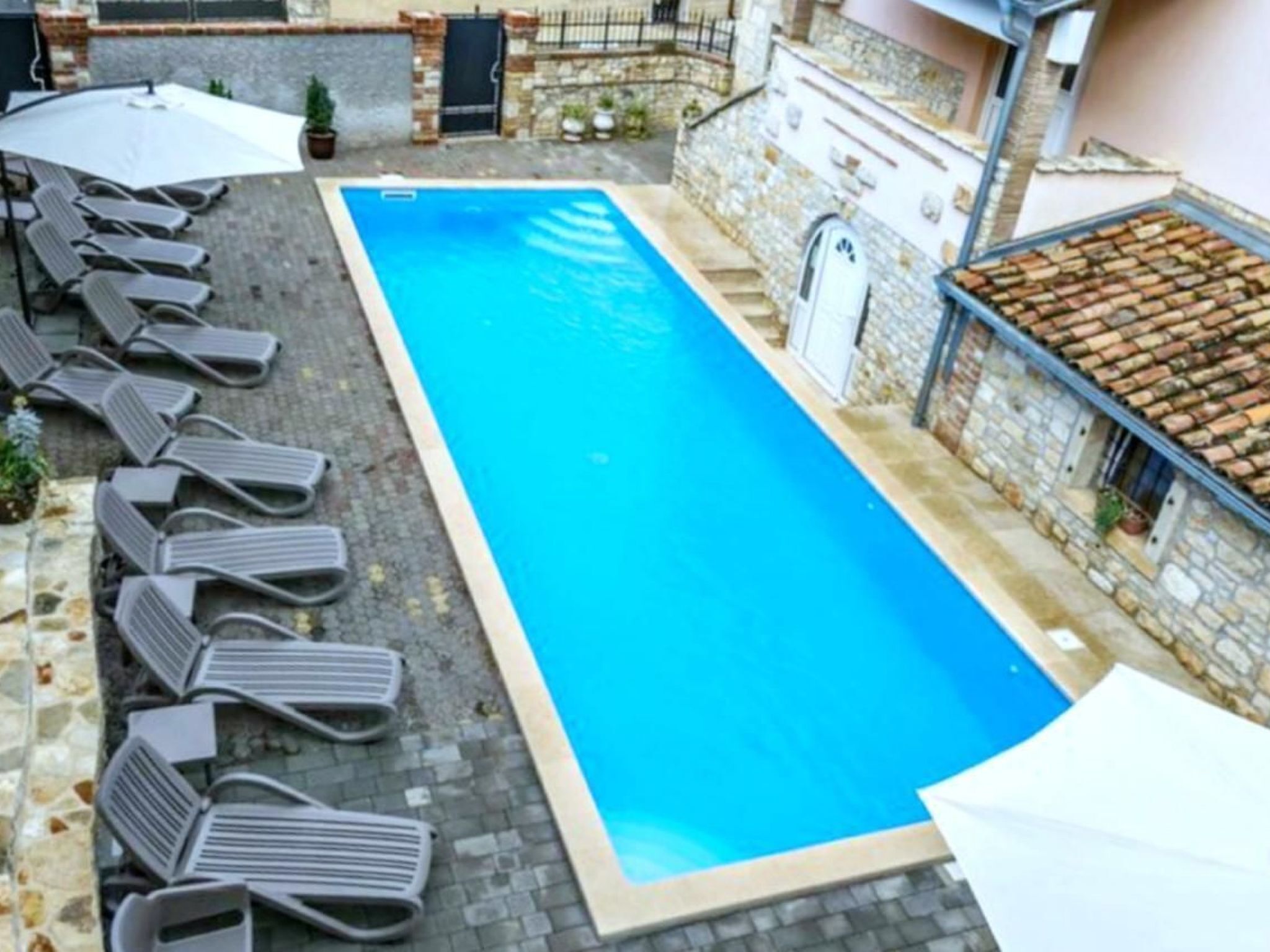 A rectangular pool with lounge chairs and umbrellas, surrounded by stone walls and a tiled roof.