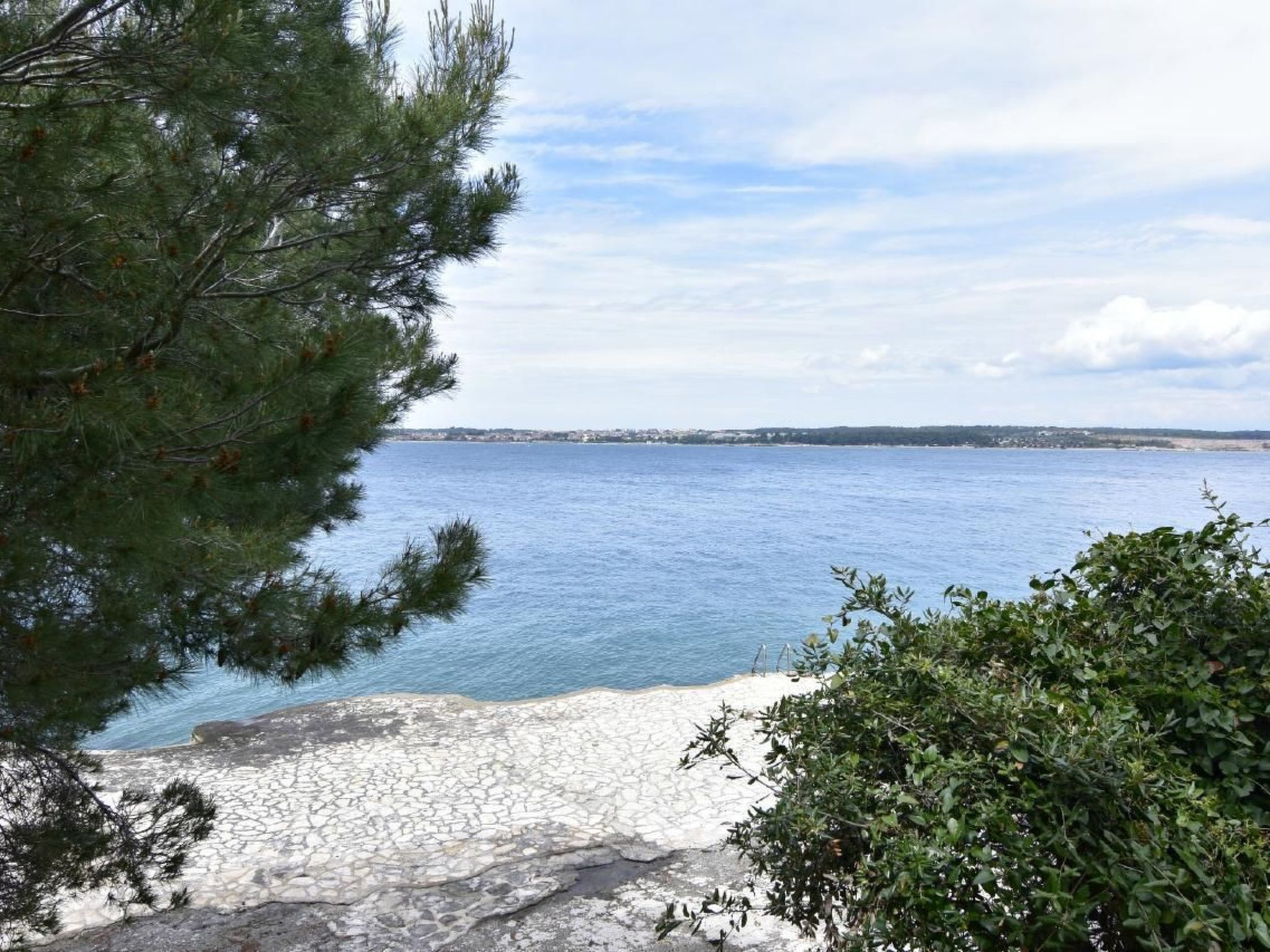 Une vue sur la côte, avec un rivage rocheux, un ciel dégagé et des bâtiments situés au loin.