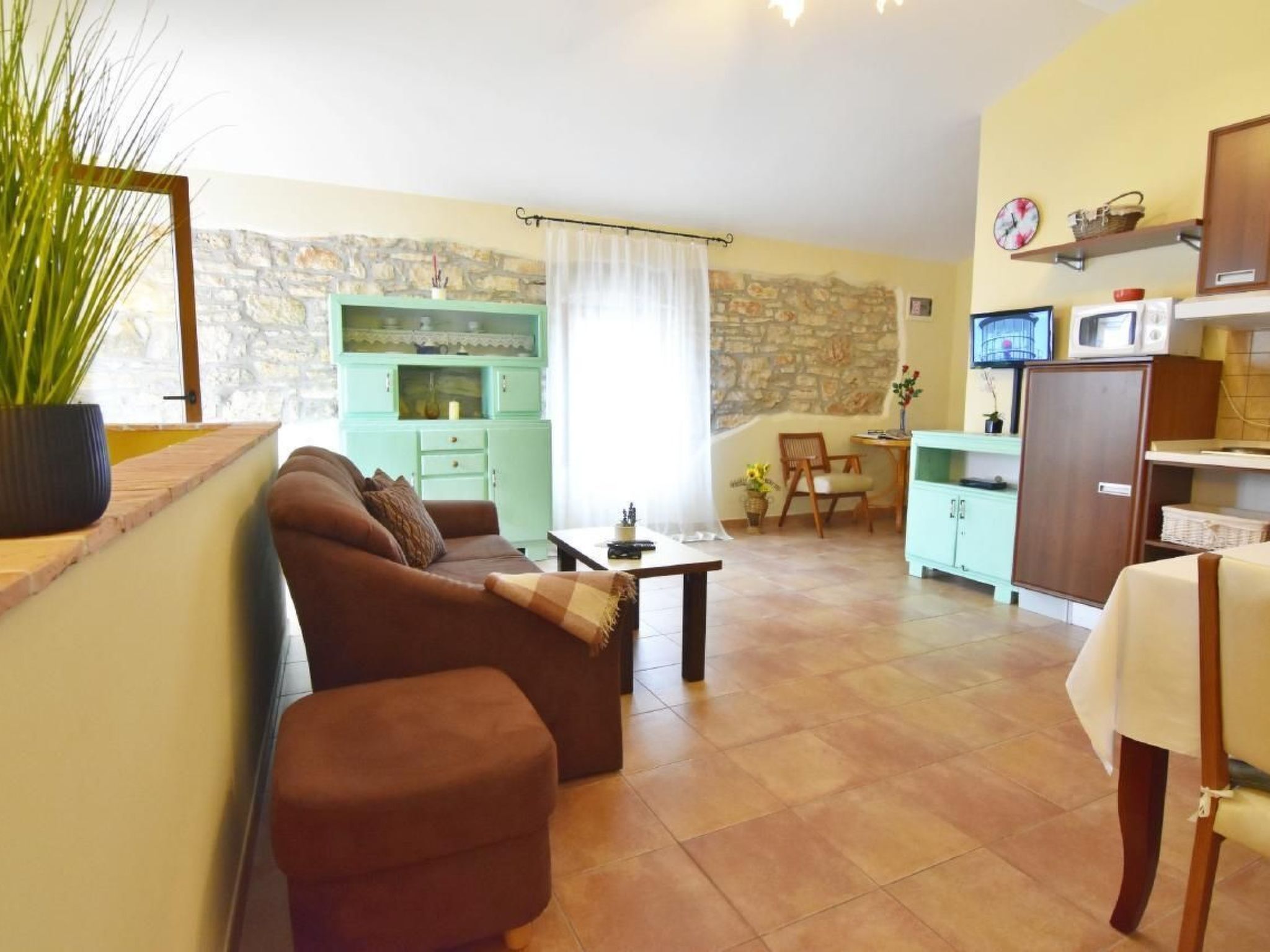 A cozy living room with a brown sofa, a small table, and a stone wall. There is a kitchen area with a microwave and a cabinet.