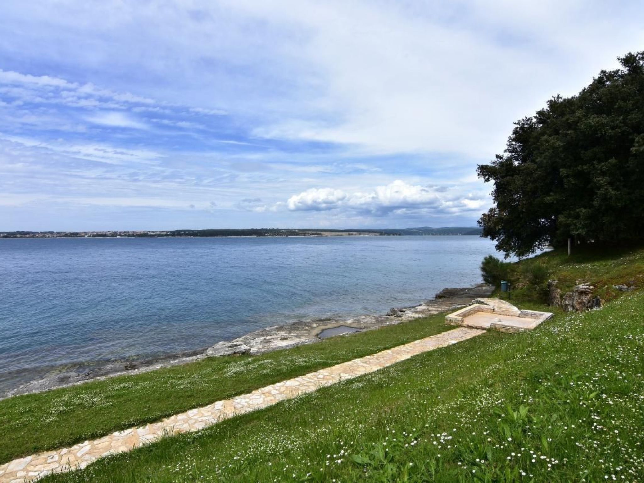 Eine Küstenlandschaft mit einem steinernen Weg, der zu einer Wiese am Wasser führt.