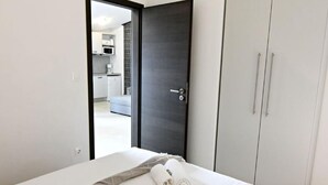 Hotellihuone, jossa on sänky, vaatekaappi ja avoin ovi, joka johtaa pieneen keittiötilaan.