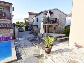 Ein Poolbereich mit Liegestühlen und einem kleinen Tisch, ein Steinhaus mit einem Balkon sowie ein geparktes Auto in der Nähe.