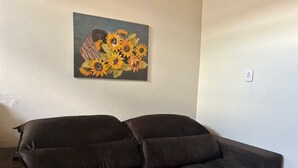 A dark brown sofa in a room with a painting of sunflowers on the wall. - Tiny house with air conditioning (Dourados)