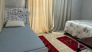 A bedroom with two beds, a white headboard with character decals, a red and gold patterned rug, and a window with beige curtains. - Tiny house with air conditioning (Dourados)