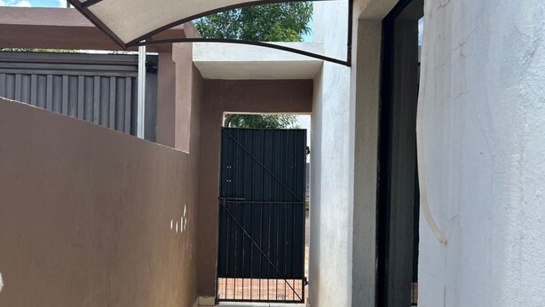 A narrow, tiled corridor with a large, beige awning providing shade. A black gate is visible at the end of the corridor. - Tiny house with air conditioning (Dourados)