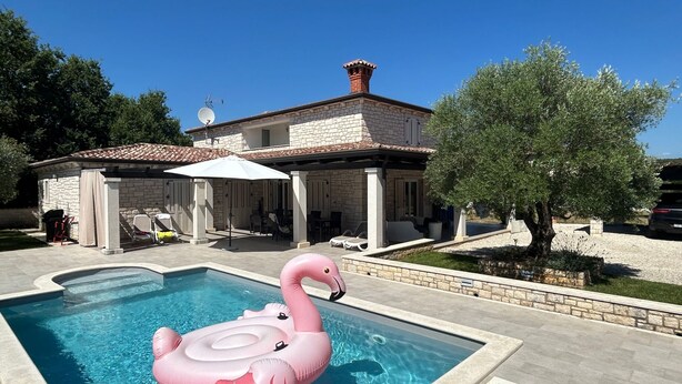 Una piscina con un flotador de flamenco rosa, un patio techado y una casa de piedra con techo de tejas.