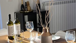 Una mesa de comedor dispuesta con platos, cubiertos y copas de vino, con un jarrón y ramas decorativas en el centro.