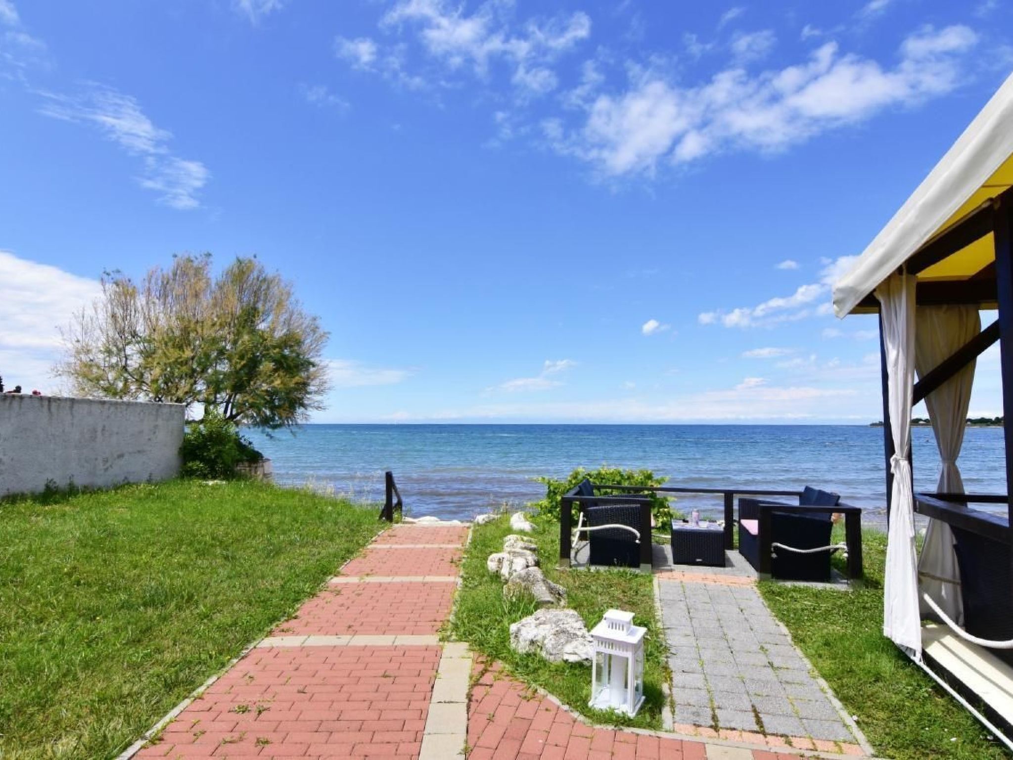 A seaside patio with a brick pathway leading to outdoor furniture and a white lantern.