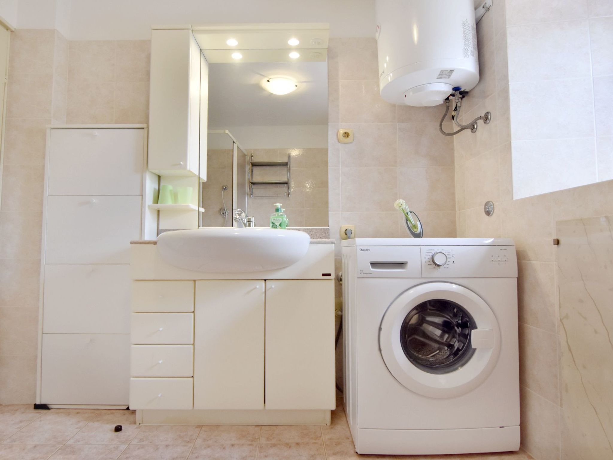 A modern bathroom with a sink, mirror, cabinet, and a front-loading washing machine.