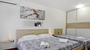 A hotel room with two beds, patterned bedspreads, a painting on the wall, a mirror, and a TV. - in Murine mit Großer Terrasse by Interhome (Umag/Murine)