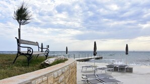 Eine Terrasse am Meer mit einer Bank, Liegestühlen und Sonnenschirmen.