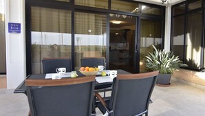 Ein Essbereich mit Tisch und Stühlen, einer Topfpflanze und Blick ins Innere durch eine Glastür.