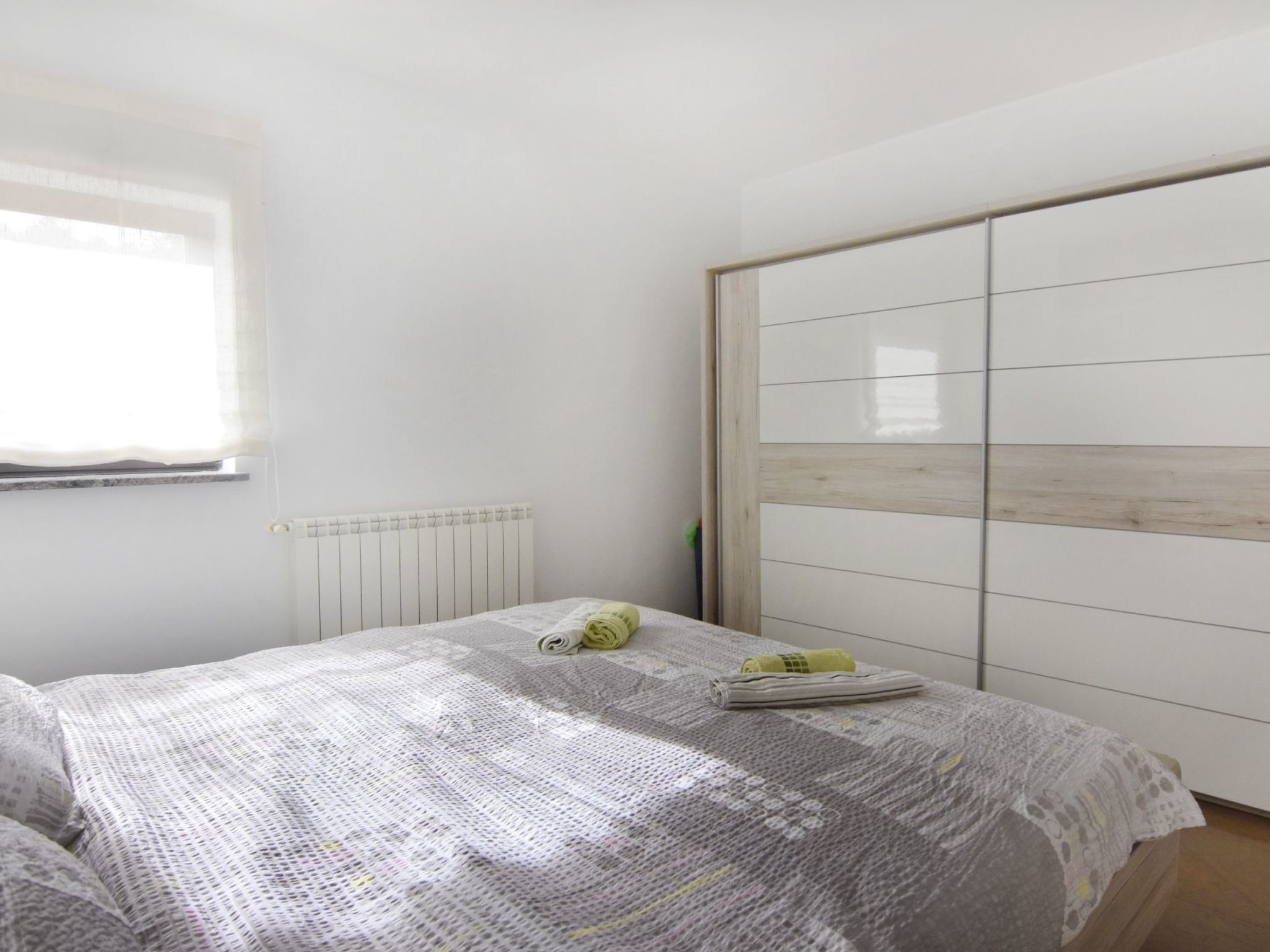 A bedroom with a bed, a radiator, a window, and a wardrobe.