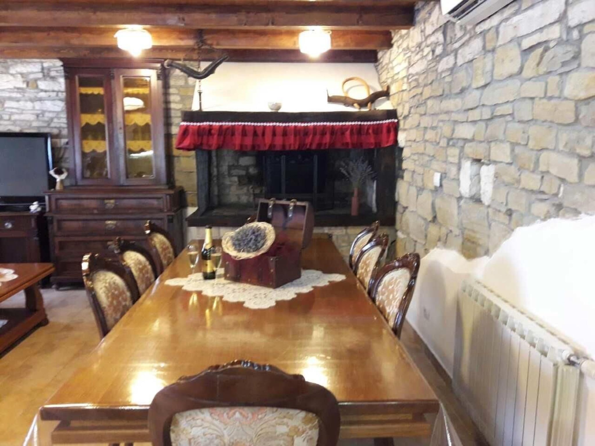 Een eetgedeelte met een lange houten tafel, stoelen, een open haard, stenen muren en een televisie.