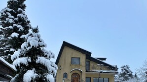 A two-story house with a snow-covered driveway and a large evergreen tree to the left. - Ferienvilla mit Garten, Grill und Terrasse by Interhome (Borkowo)