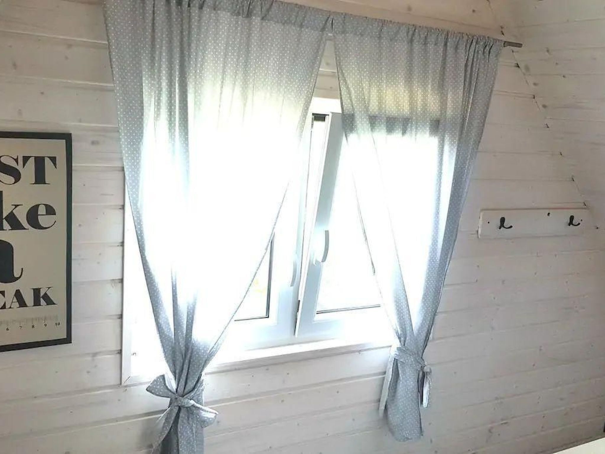 A room with a window covered by light grey curtains tied at the bottom.
