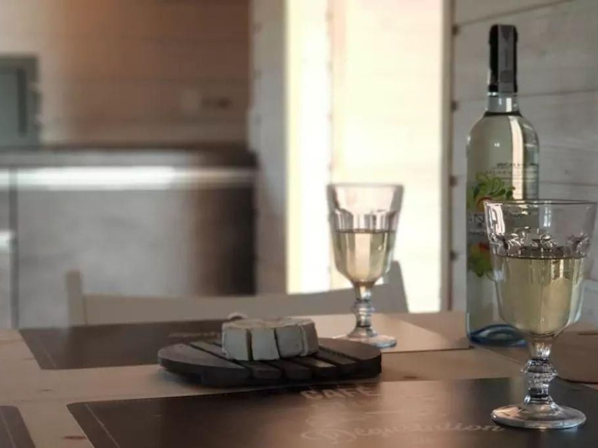A table with a bottle of white wine, a glass of white wine, and a cheese board.