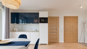 Cocina moderna con armarios azul oscuro, encimera blanca y microondas. Hay una zona de comedor con una mesa blanca y sillas azules.