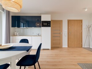 Cocina moderna con armarios azul oscuro, encimera blanca y microondas. Hay una zona de comedor con una mesa blanca y sillas azules.