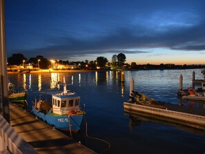 A docked boat with a cabin and a blue cover marked "MEC-42" at a marina with calm water and distant shoreline lights. - Alvista Apartments mit Meerblick by Interhome (Pierwoszyno)