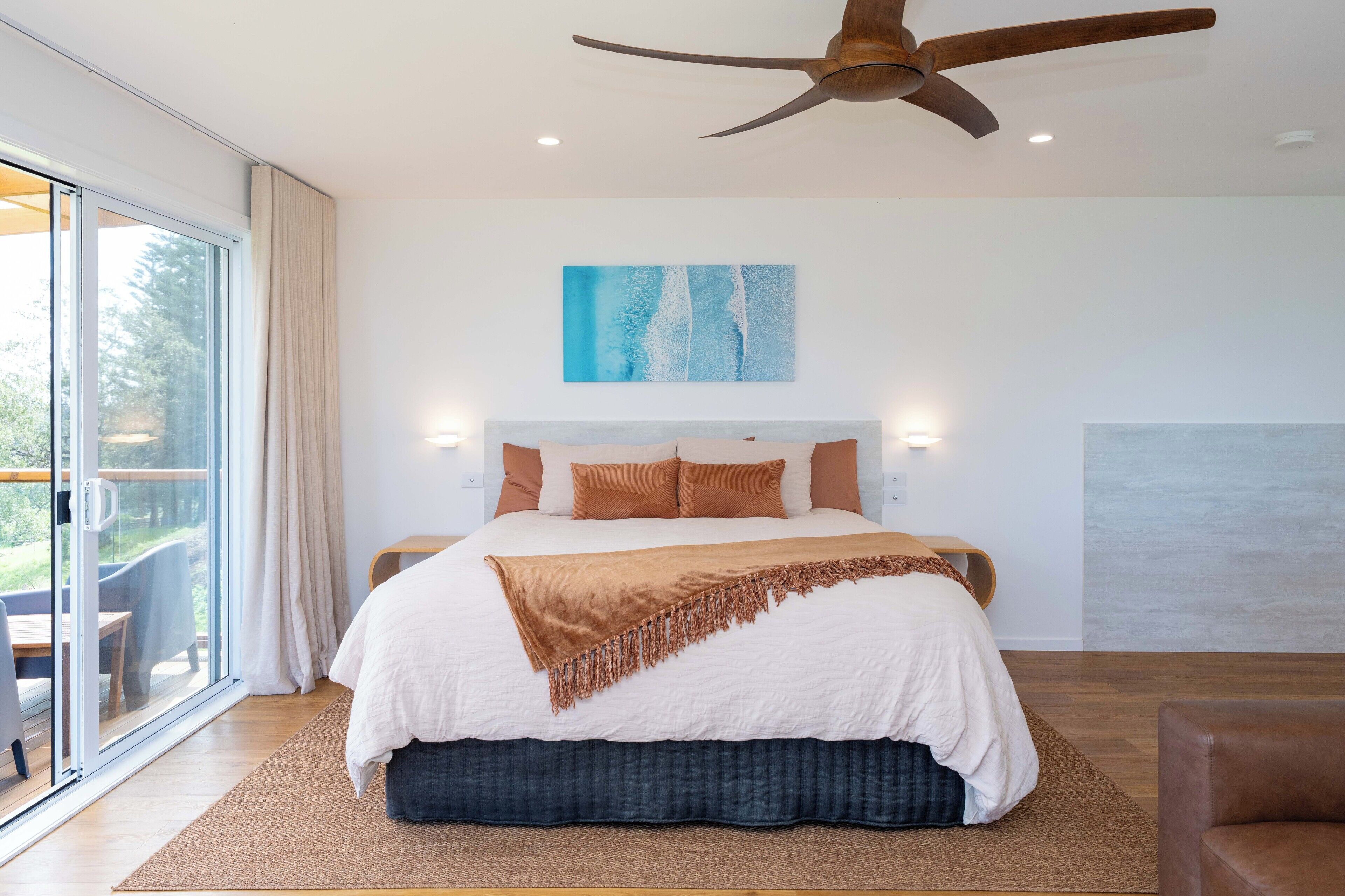 Ein modernes Schlafzimmer mit einem großen Bett, einem Deckenventilator und Blick durch eine Schiebetür.