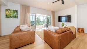 A modern living room with two leather sofas, a flat-screen TV, and a large window with curtains.