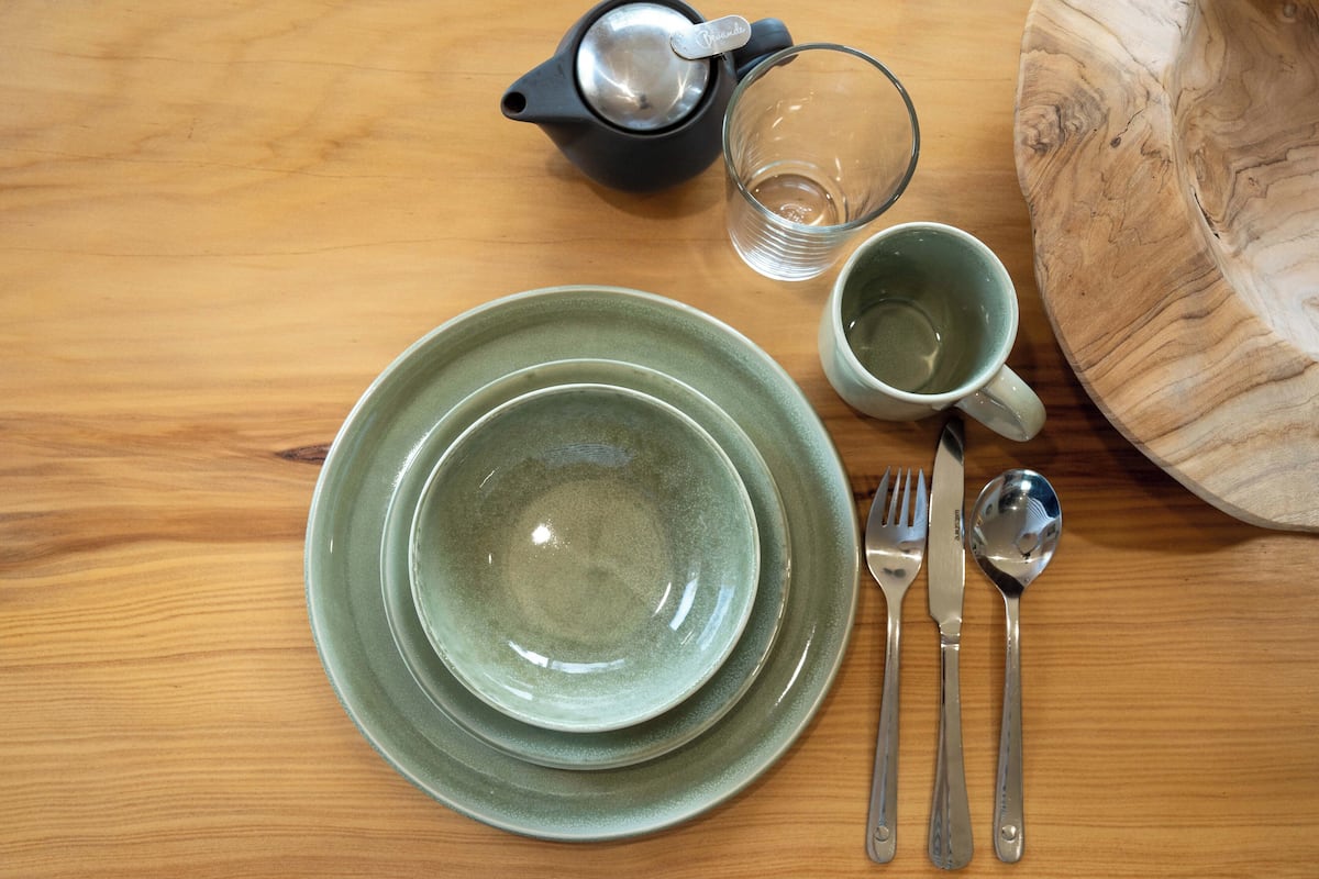 A wooden table with a set of green plates, a glass, a cup, and cutlery.